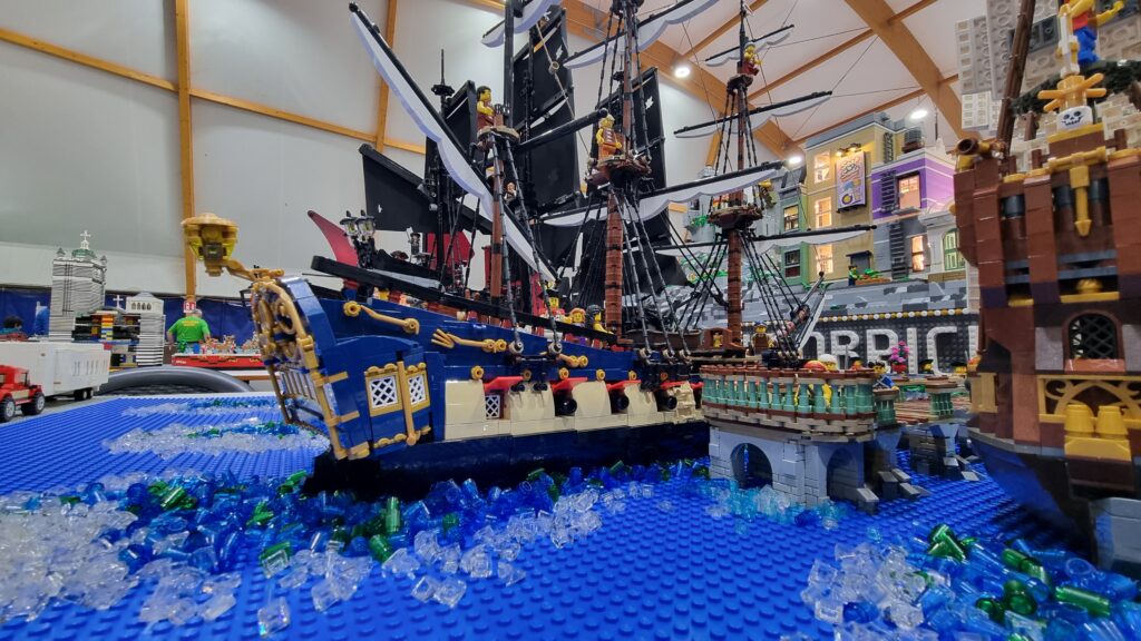 Nave blu e bianca con vele scure, accanto al molo del diorama.