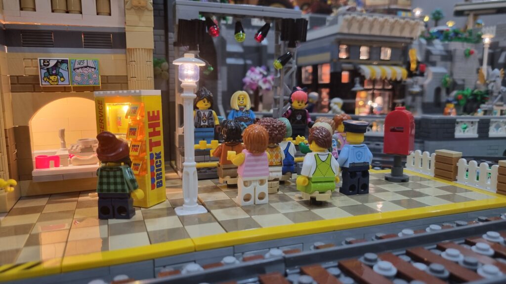 Minifigure su un piccolo palco davanti a un pubblico in miniatura, accanto alla ferrovia.