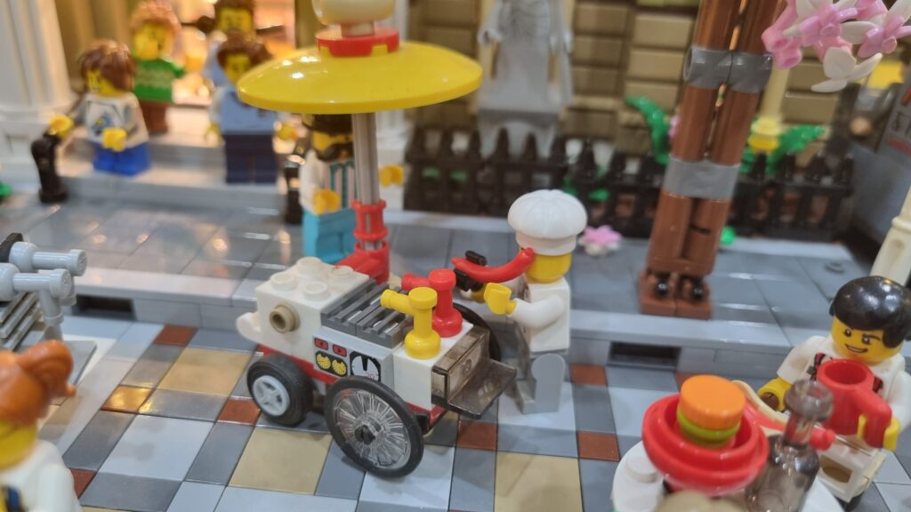 Minifigure dietro un carretto degli hot dog con ombrellone giallo.