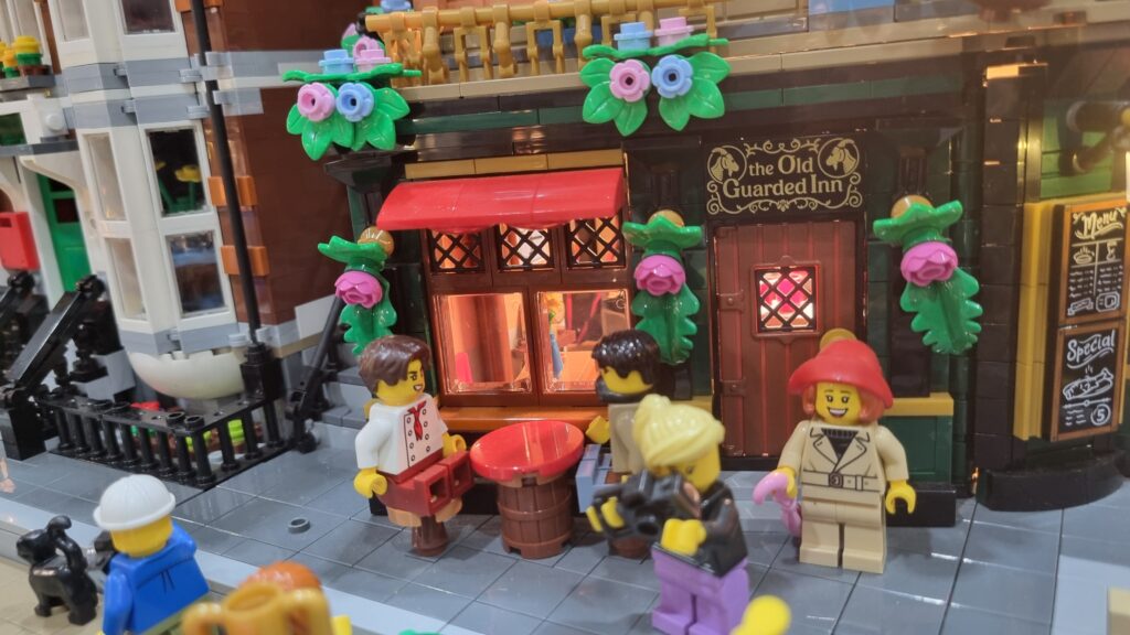Locanda con vetrina illuminata, insegna The Old Guarded Inn e minifigure attorno a un tavolo.