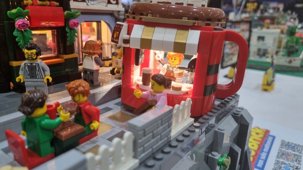 Chiosco rosso a forma di tazza con interno illuminato e minifigure al tavolino.